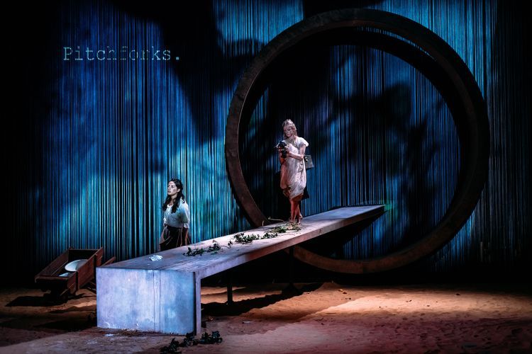 Actors walking down a long platform on stage, with a large video projected background behind them